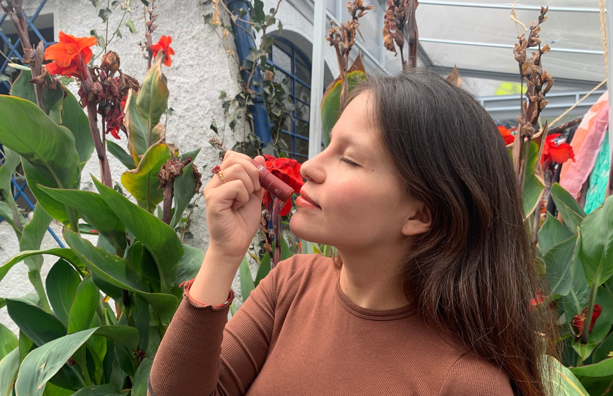 Mujer Aplicandose labial Lulú Rojo con plantas detrás de ella