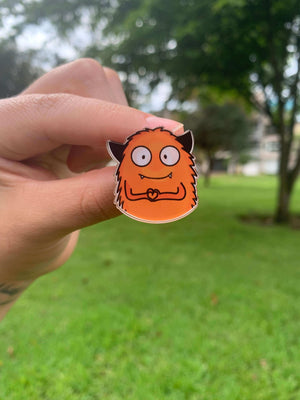 Pin monstruo naranja haciendo un corazon con sus manos